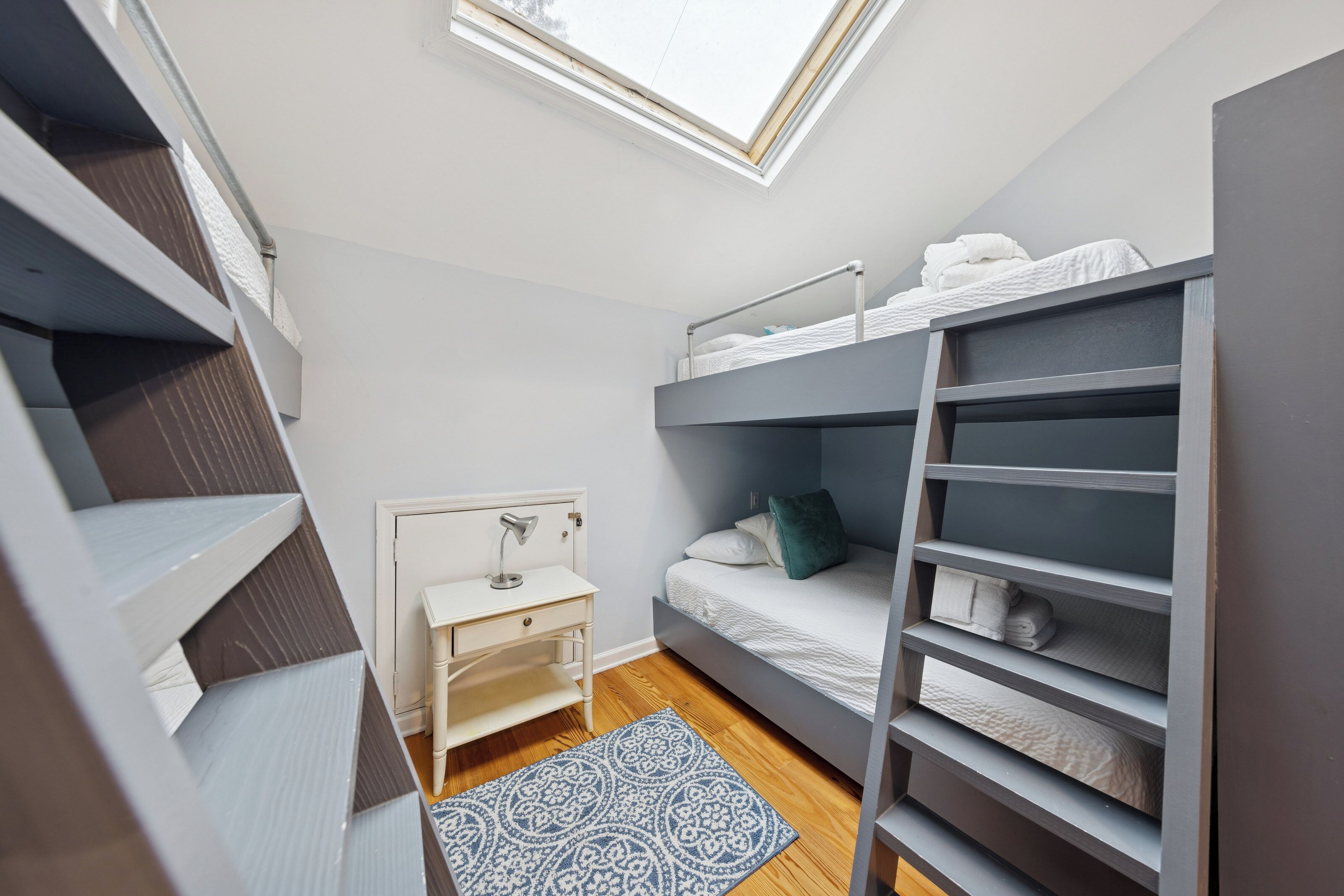 Un dormitorio pequeño con una cama litera, un escritorio y un tragaluz.