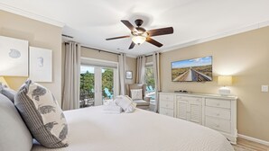 A bedroom with a large bed, a ceiling fan, a TV, and a view of the outdoors. - 7 Strath Court @ Palmetto Dunes | Private Pool | Pet Friendly | Cozy Loft | Spacious Kitchen (Hilton Head Island)