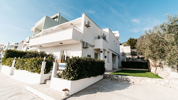 Un edificio moderno blanco con techo plano, un balcón y un cartel que indica que es un apartamento.