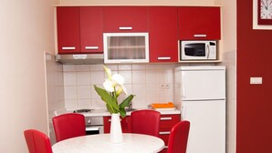 Una cocina compacta con armarios rojos, un microondas blanco, un refrigerador blanco y una mesa de comedor redonda con sillas rojas.