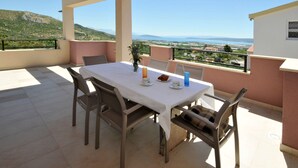 A balcony with a table set for two, chairs, a vase with flowers, and a view of a coastal landscape. - Villa Rimac in Kastel Stafilic mit Garten, Grill by Interhome (Kaštel Novi)