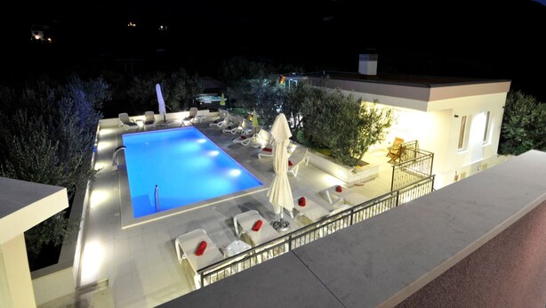 A swimming pool with lounge chairs and umbrellas, surrounded by a modern building with a balcony. - Villa Rimac in Kastel Stafilic mit Garten, Grill by Interhome (Kaštel Novi)