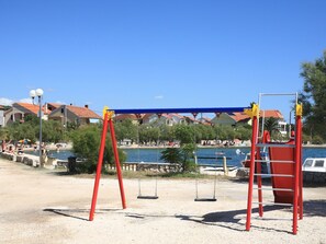 A beach with a swing set, a pool, and houses in the background. - Sonnige Wohnung "Bepo" mit Blick auf das Wasser by Interhome (Zadar/Bibinje)
