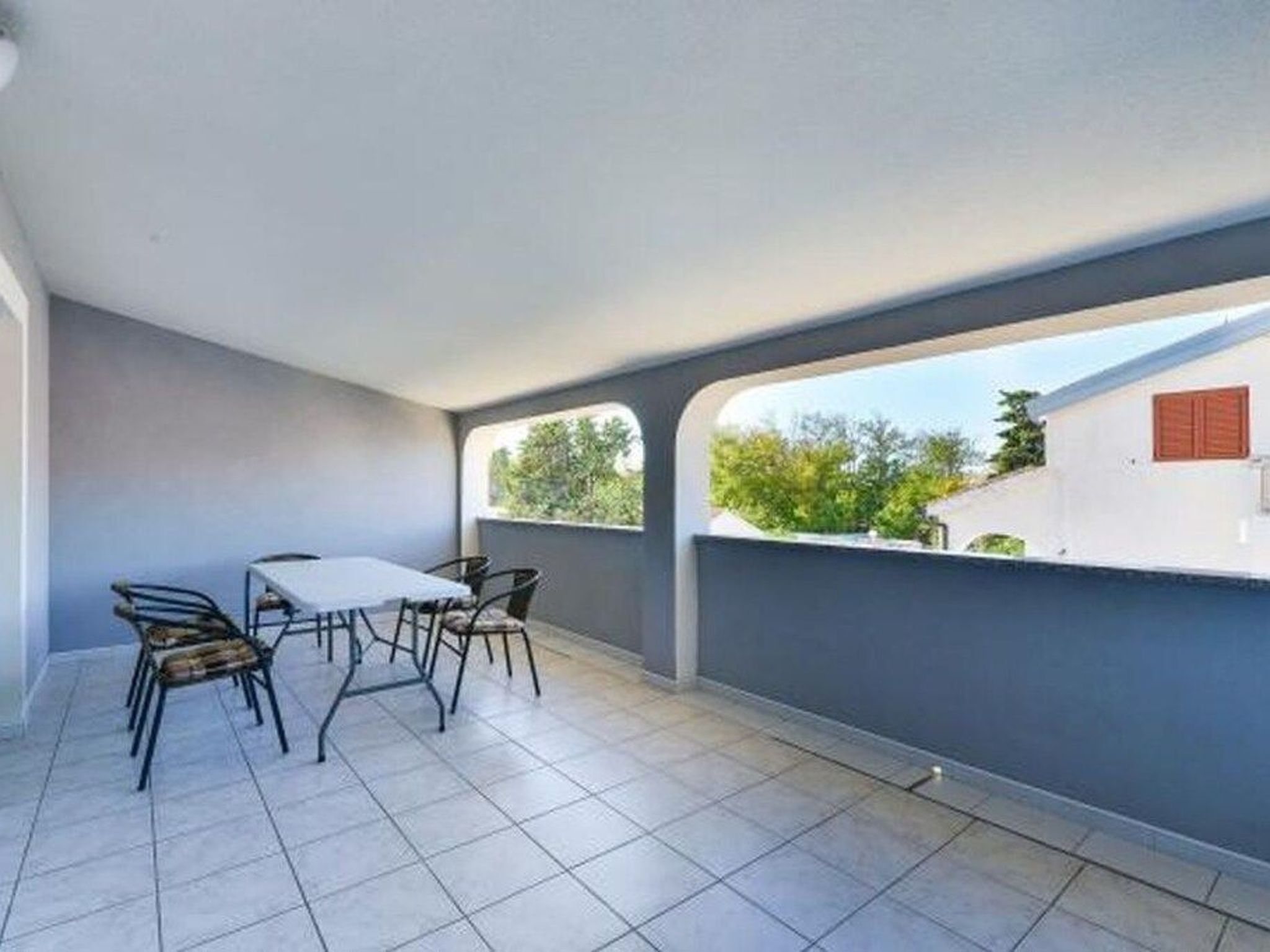 A balcony with a table and chairs, a tiled floor, and a view of greenery and buildings.