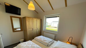 Quarto com duas camas, um guarda-roupa de madeira, um espelho, uma televisão e janela com vista para o exterior.