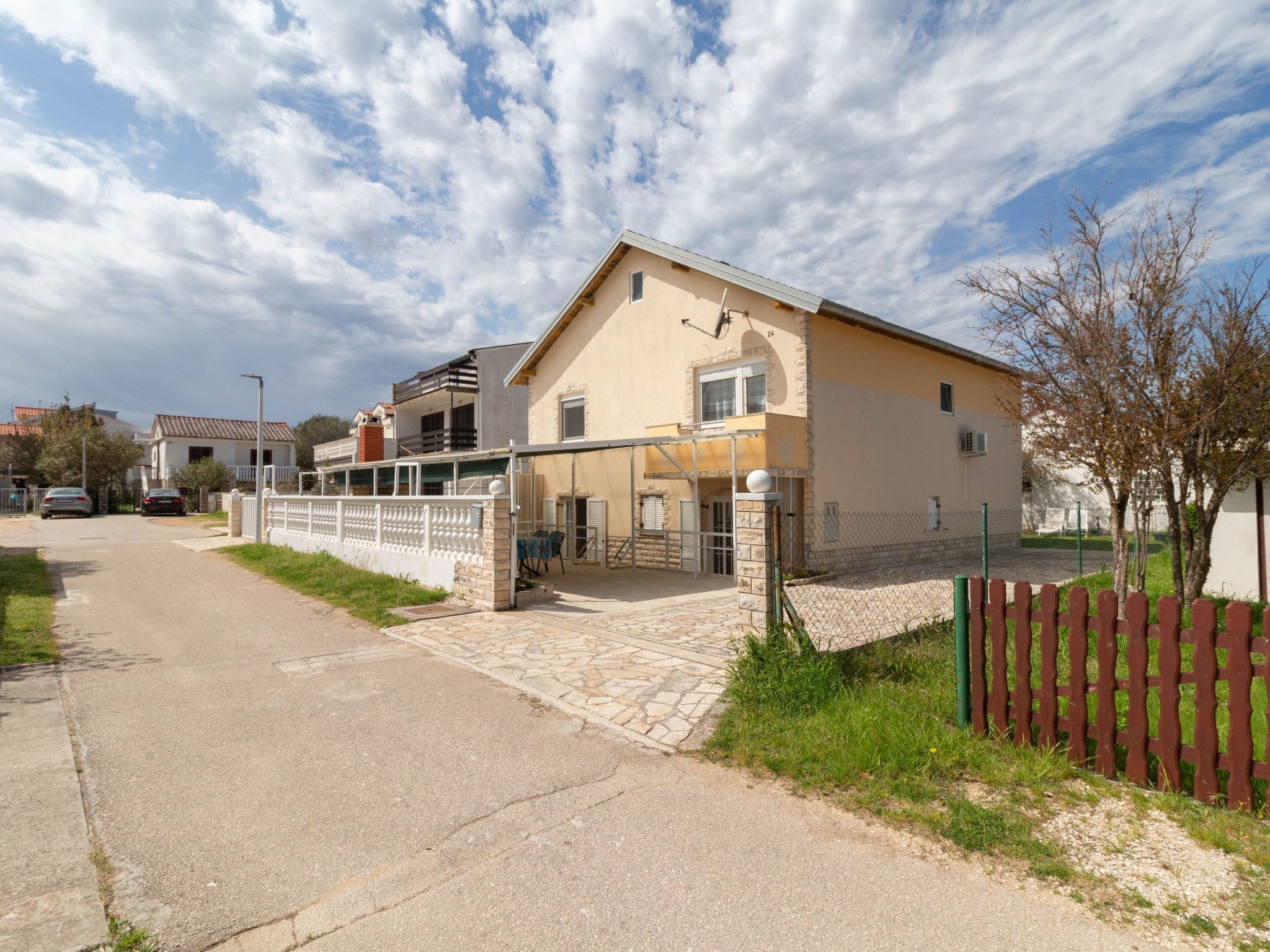 A two-story house with a paved driveway, a fenced yard, and a small garden area.