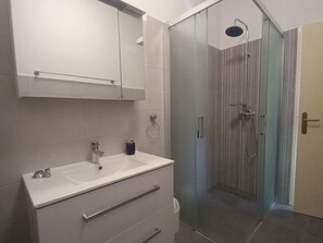 Ett modernt badrum med en dusch som är avskärmad med glasväggar, ett vitt handfat med tillhörande skåp och en spegel ovanför handfatet.