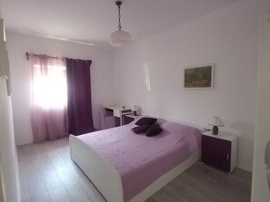 Ett sovrum med en säng, ett skrivbord, en stol, en lampa och en tavla på väggen.