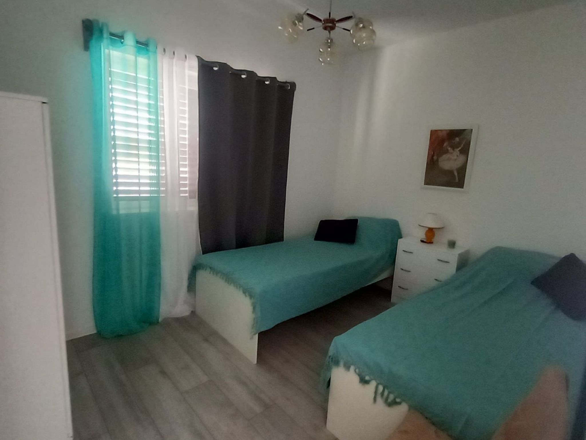 Ein Schlafzimmer mit zwei Einzelbetten, einer weißen Kommode, einem Deckenventilator und einem Fenster mit Vorhängen.