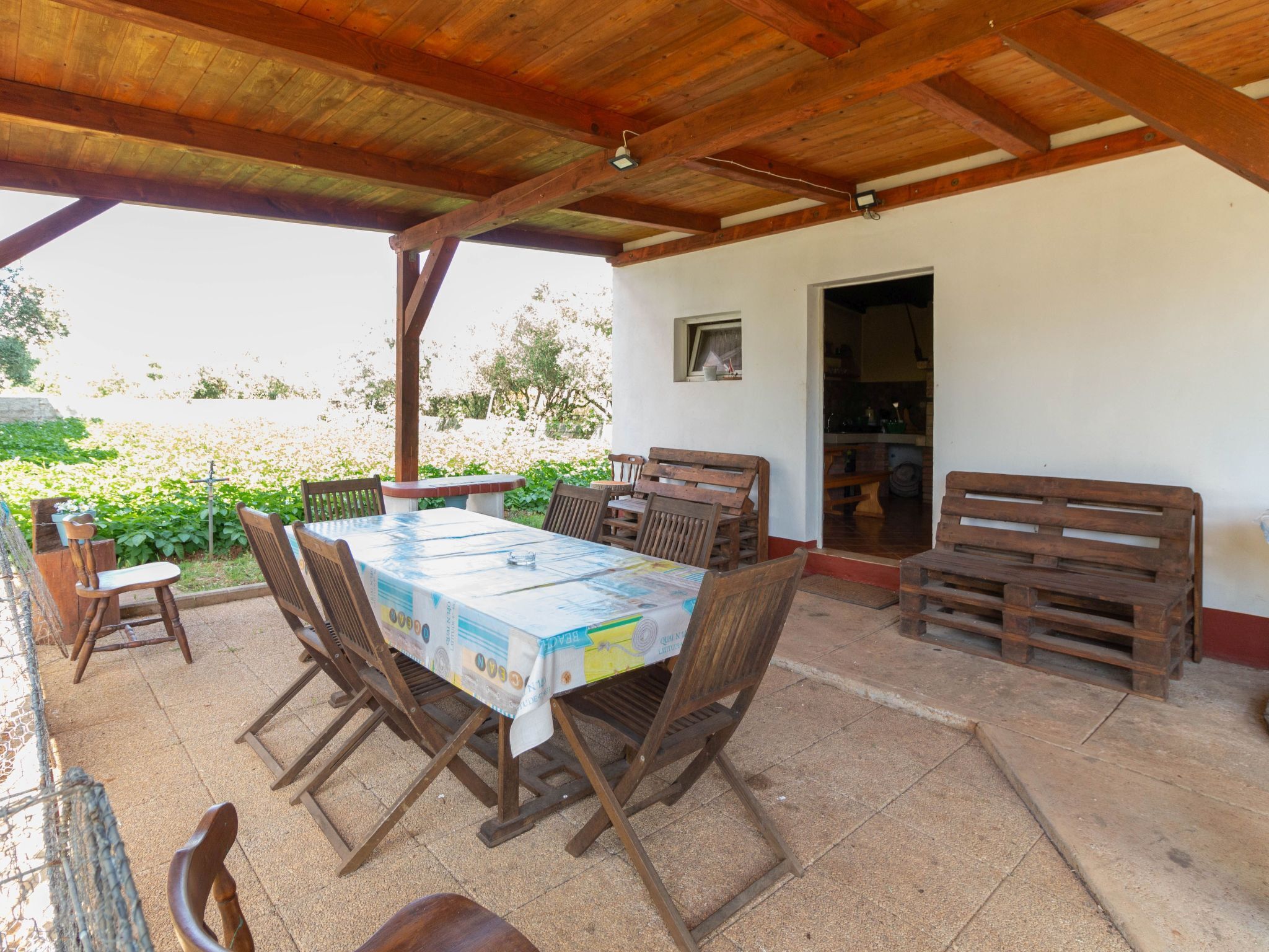 An outdoor patio with a wooden table and chairs, a covered area with a wooden ceiling, and a view of a garden.