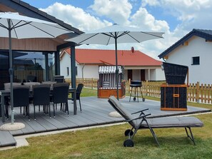 Een terras buiten met een eettafel en stoelen, een barbecue en een lounge stoel.