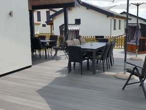 Een terras buiten met een eettafel en stoelen, een barbecue en een houten omheining.