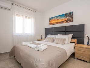 Ein modernes Schlafzimmer mit einem großen Bett, einem Kopfteil, einem Nachttisch, einer Wandlampe und einem Sonnenuntergangsbild.