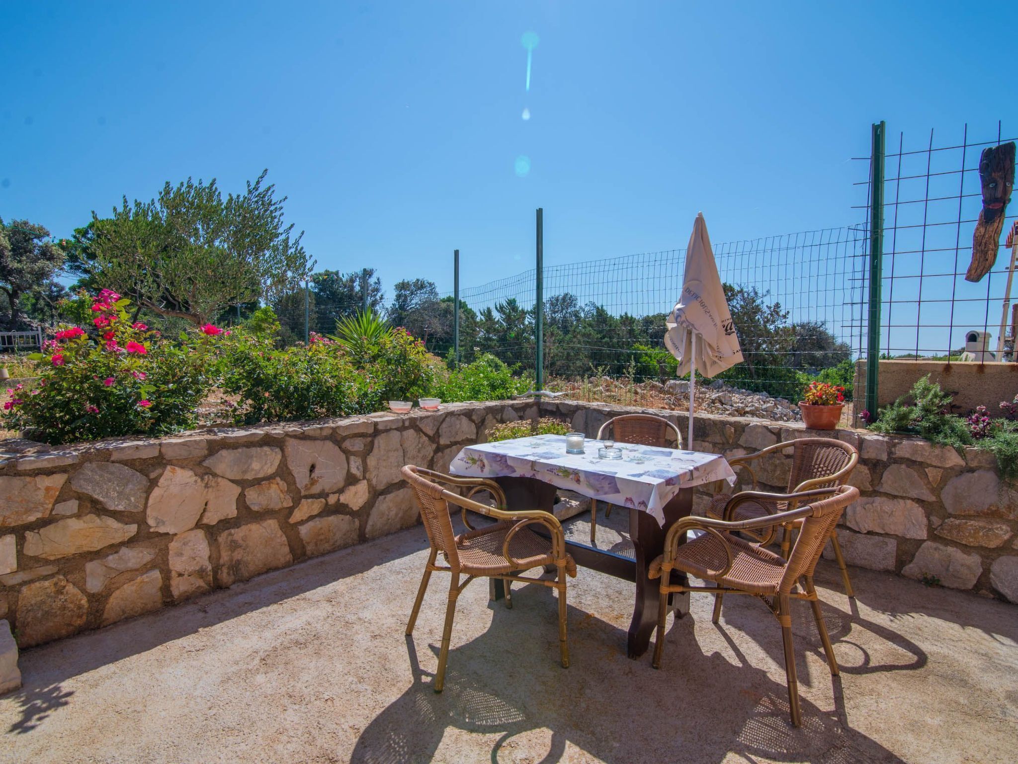 An outdoor patio with a stone wall, wicker chairs, a table with a tablecloth, and a potted plant.