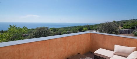 A balcony with a view of the sea, a wicker sofa, and a small table.