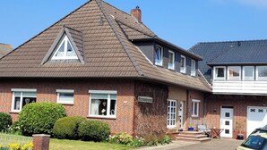 Ein zweistöckiges Backsteinhhaus mit Satteldach, einer kleinen Veranda und einer sichtbaren Garagentür.