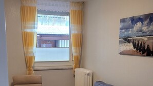 Ein Wohnzimmer mit einem beigen Sessel, einem grauen Sofa, einem weißen Couchtisch und einem Bild mit einer Strandansicht.