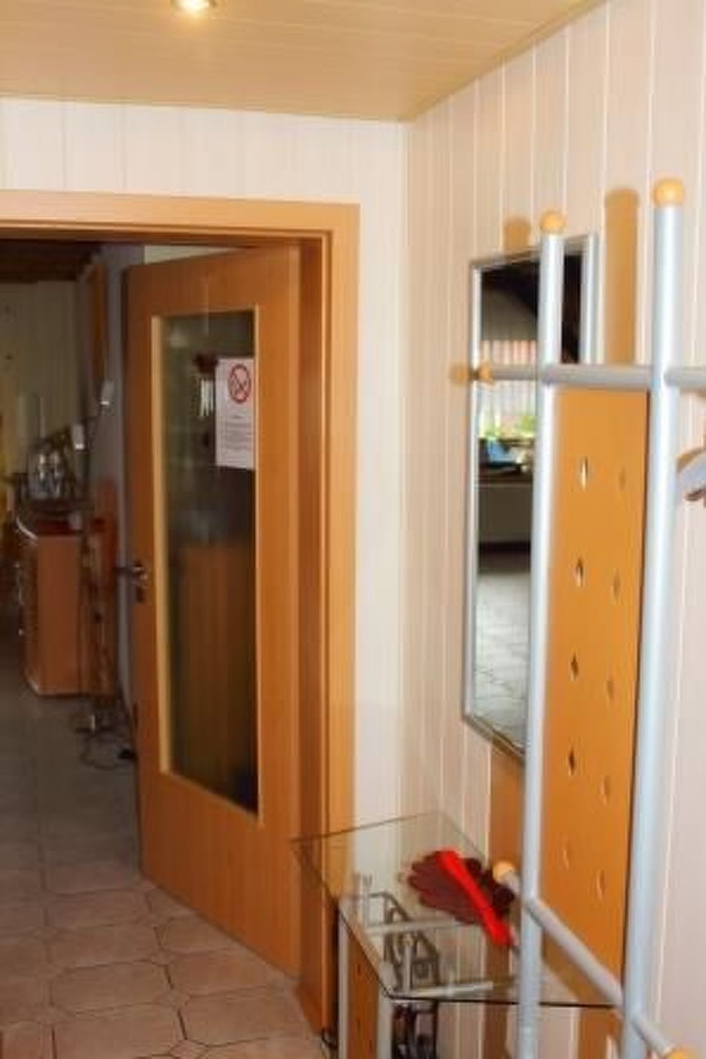 A hotel corridor with a wooden door, a glass cabinet with a red object, and a mirror with a wooden frame.