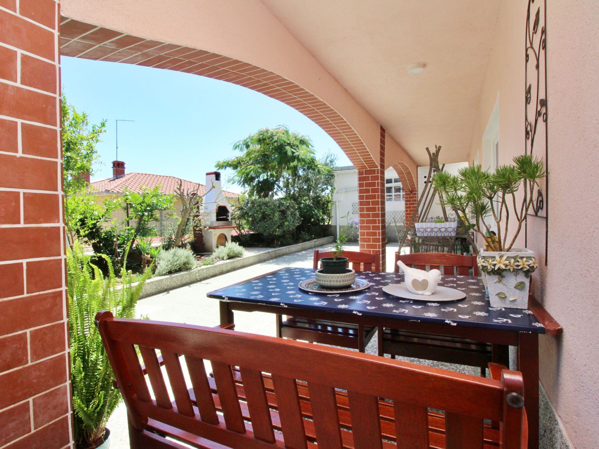 A patio with a table set for two, a bench, and a potted plant.