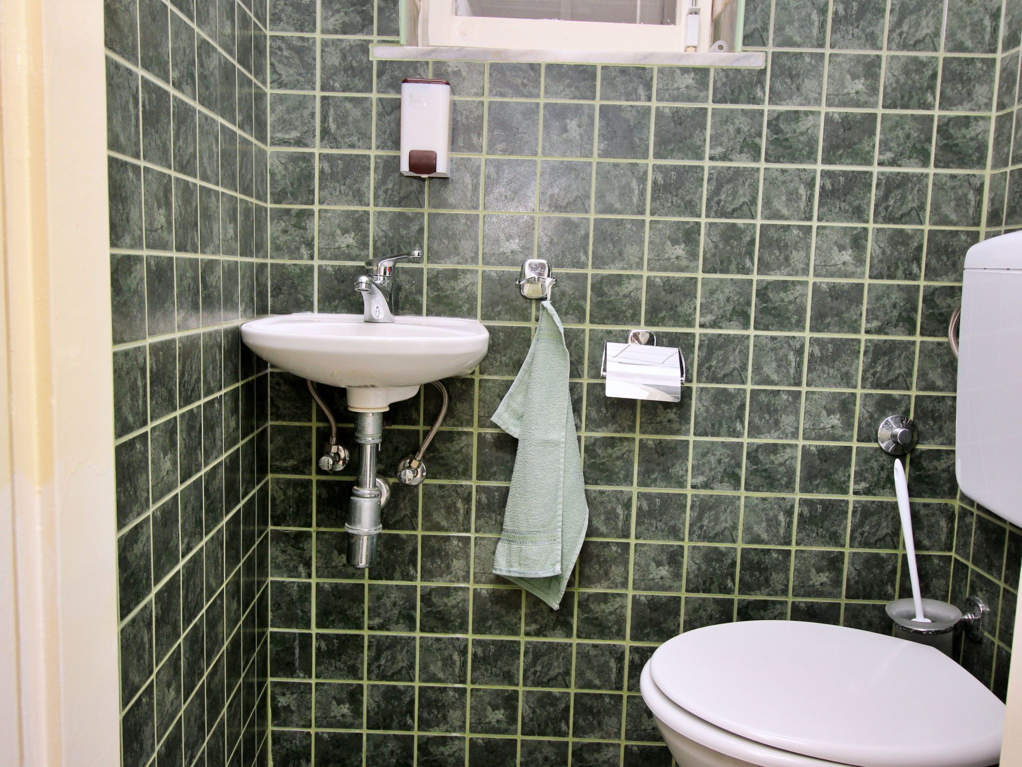 A bathroom with a white sink, green tiled walls, a toilet, and a towel hanging on a rack.