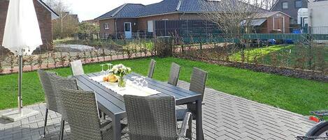 An outdoor patio with a table set for dining, surrounded by wicker chairs.