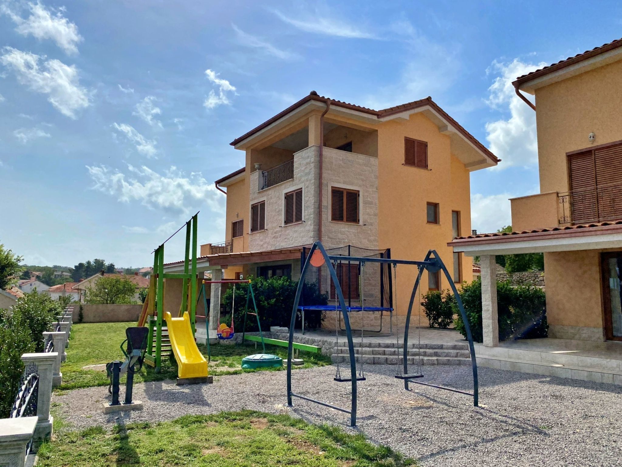 Un'area giochi con altalene e uno scivolo, circondata da un edificio con un balcone e una zona riparata.