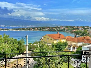 Une ville côtière avec des maisons donnant sur une baie, un ciel dégagé et une chaîne de montagnes à l’horizon.