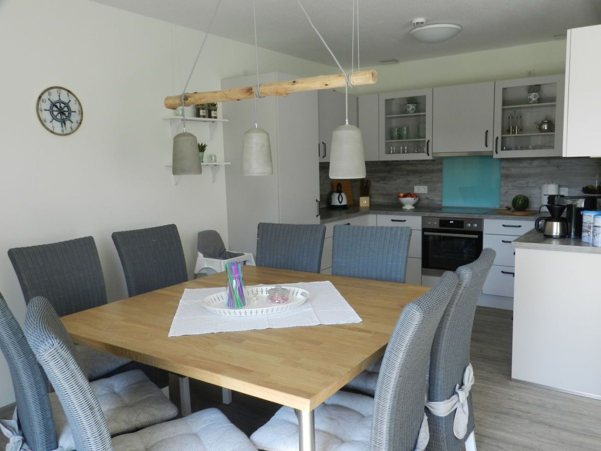 A modern kitchen with white cabinets, a wooden dining table, and grey upholstered chairs.