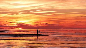 En solnedgång över en strand med två silhuettliknande figurer som står på stranden.