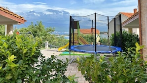 Een achtertuin met een trampoline, een speeltoestel en uitzicht op zee.