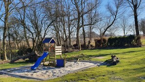 Een speeltuin met een glijbaan en klimconstructies, omringd door gras en bomen.