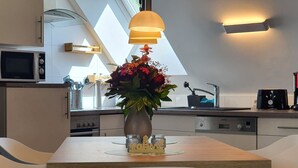 A modern kitchen with a dining area, featuring a wooden table, white chairs, a vase with flowers, and a microwave above the counter. - Friesenhof by Interhome (Burhave)