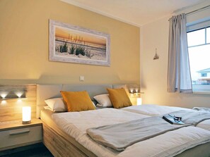 A double bed with white bedding and two pillows, a bedside table with a lamp, and a wall-mounted painting of a beach scene. - in Burhave mit Großer Terrasse by Interhome (Burhave)