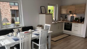 Una cocina moderna con armarios blancos, horno integrado y un comedor con mesa y sillas blancas.