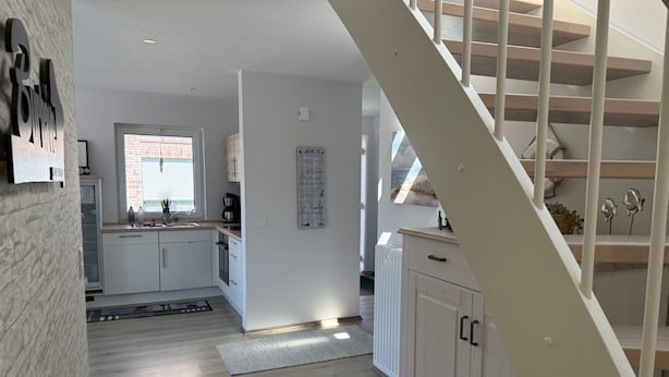 Una cocina moderna con armarios blancos, piso de madera y una escalera que sube a un nivel superior.