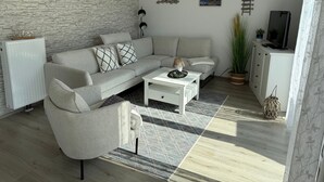 Una sala de estar moderna con un sofá gris, una mesa de centro blanca y una pared con textura de piedra.