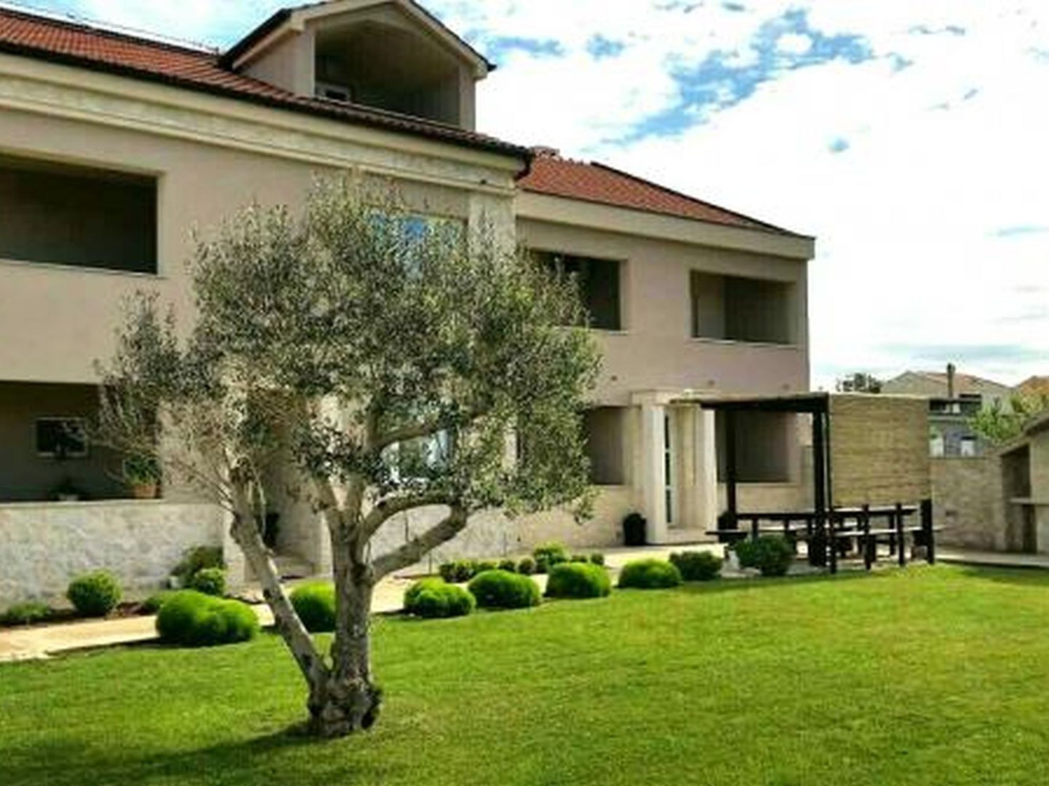Un edificio a due piani con tetto in tegole rosse, un piccolo albero nel cortile e siepi curate.