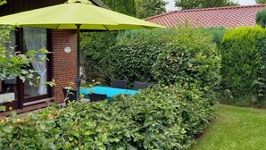 A patio area with a green umbrella, a brick wall, and a blue table. - Ferienhuus Tossens by Interhome (Burhave)