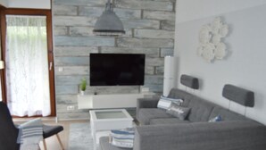A modern living room with a grey sofa, a coffee table, and a flat-screen TV mounted on a stone wall. - Ferienhuus Tossens by Interhome (Burhave)
