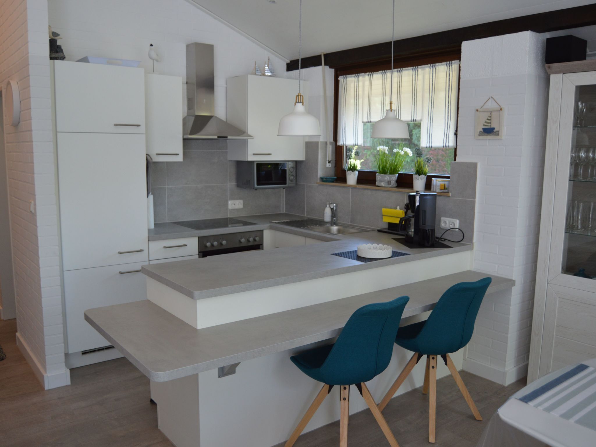 Een moderne keuken met witte kasten, een centraal eiland, twee teal-kleurige stoelen en een koffieapparaat.