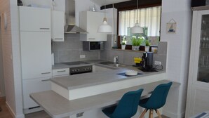 A modern kitchen with white cabinetry, a central island, two teal chairs, and a coffee machine. - Ferienhuus Tossens by Interhome (Burhave)