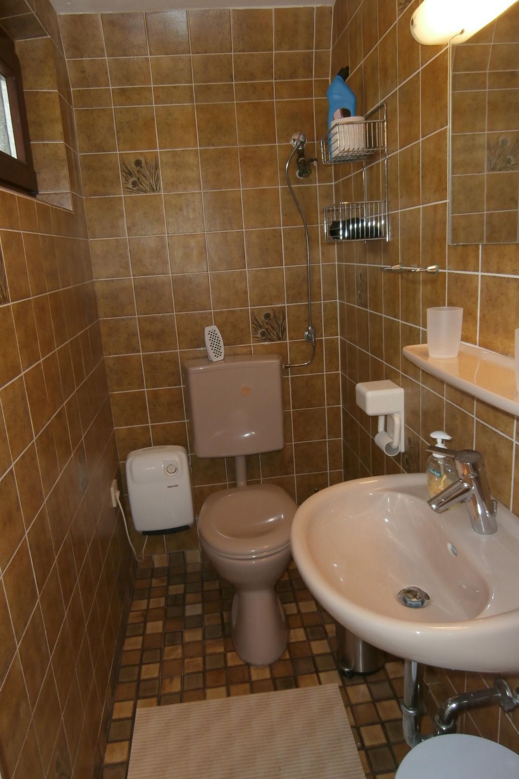 Een badkamer met bruine betegelde muren, een toilet, een wastafel en een douche.