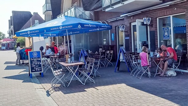 Espace extérieur aménagé avec des tables et des chaises, un parasol bleu et un panneau indicateur.