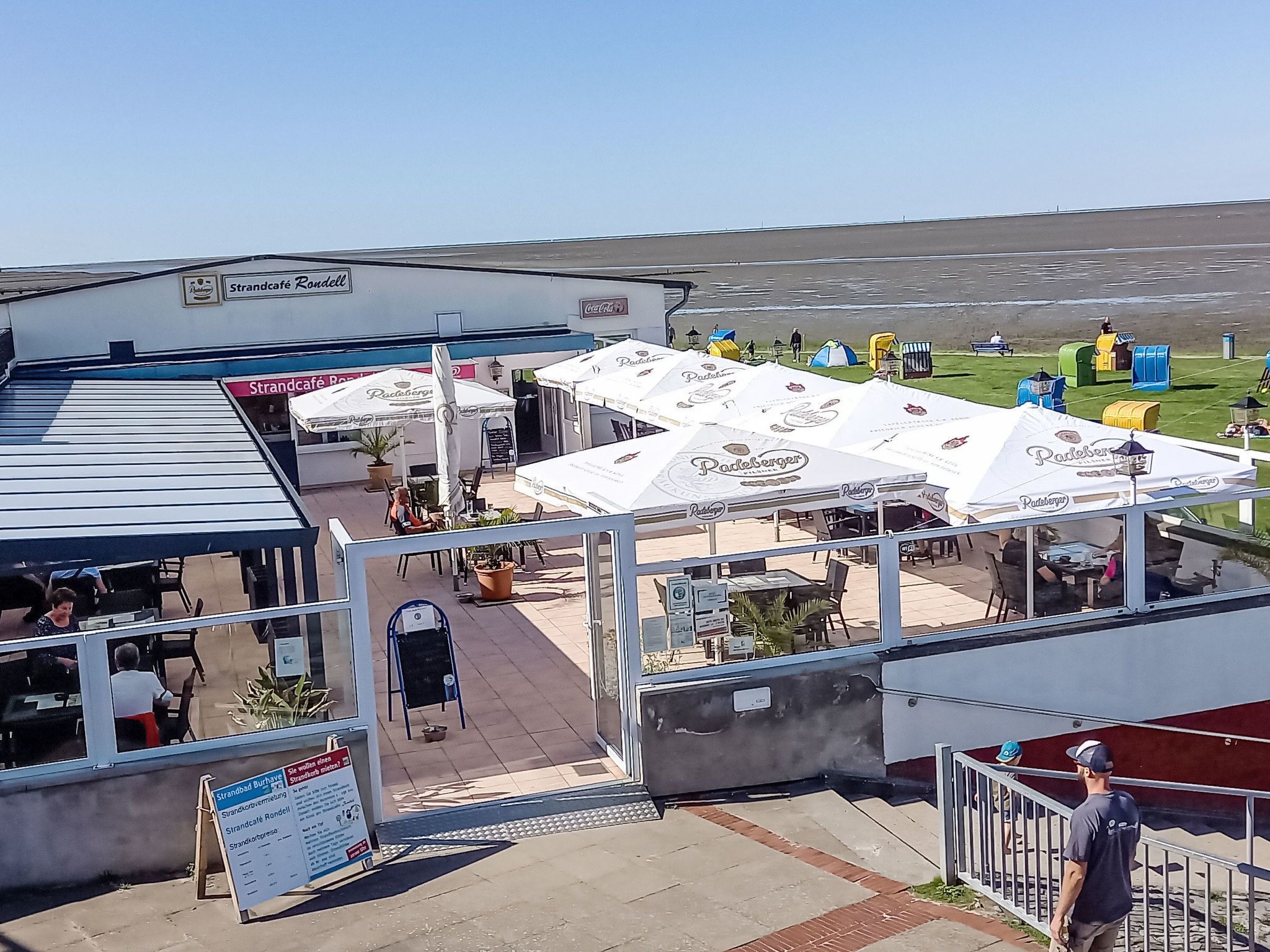 Ein Restaurant am Wasser mit Außenbereich, weißen Markisen und Blick auf das Meer.