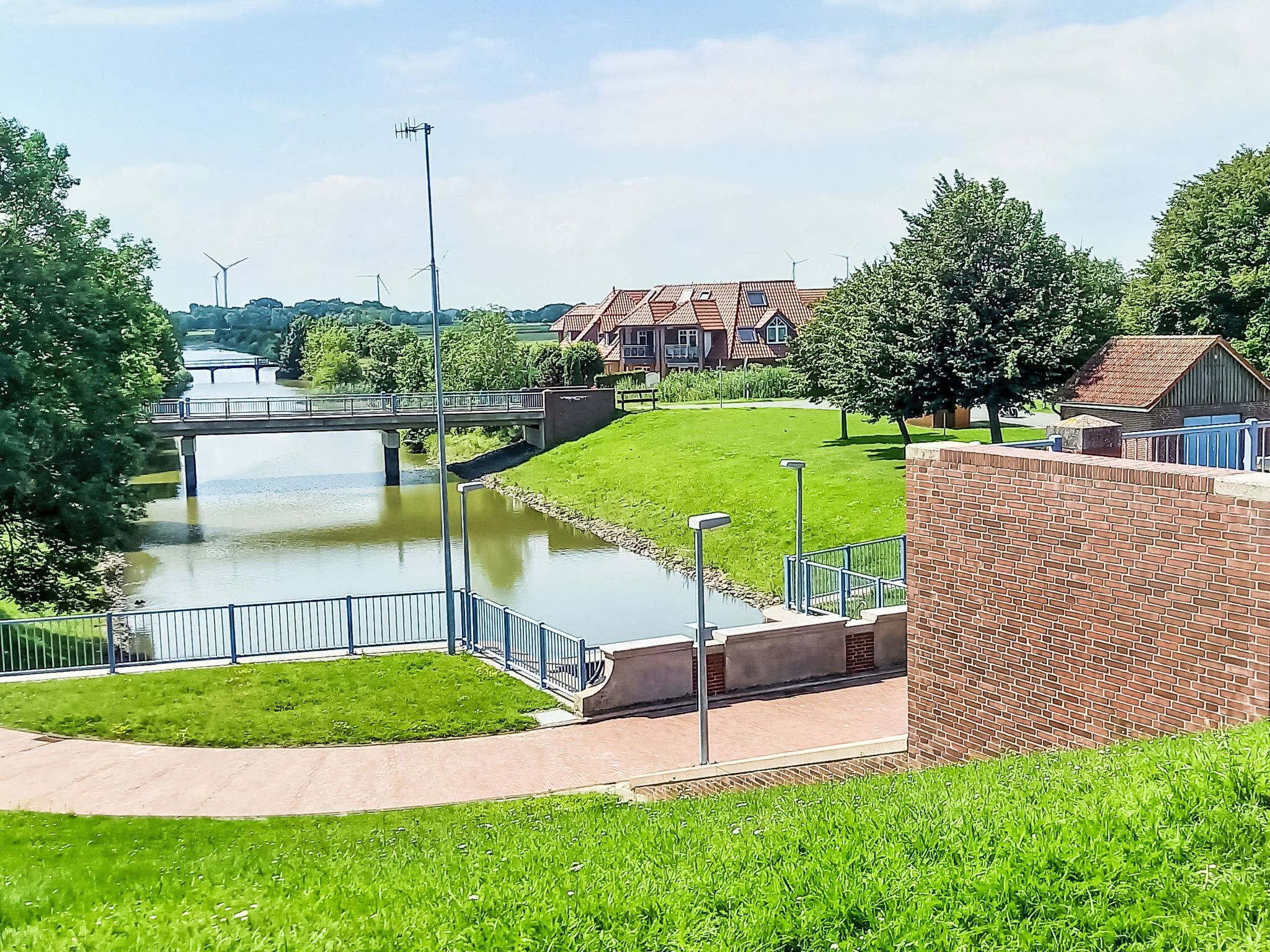 A riverside walkway with a bridge, a brick wall, and residential buildings in the background.