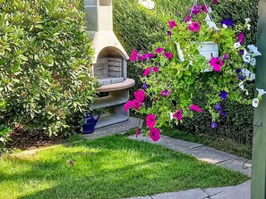 A garden with a stone bench, a blue watering can, and flowering plants.
