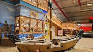 Un área de juegos con forma de barco, que incluye cubierta de madera, ventanas y un bote salvavidas.