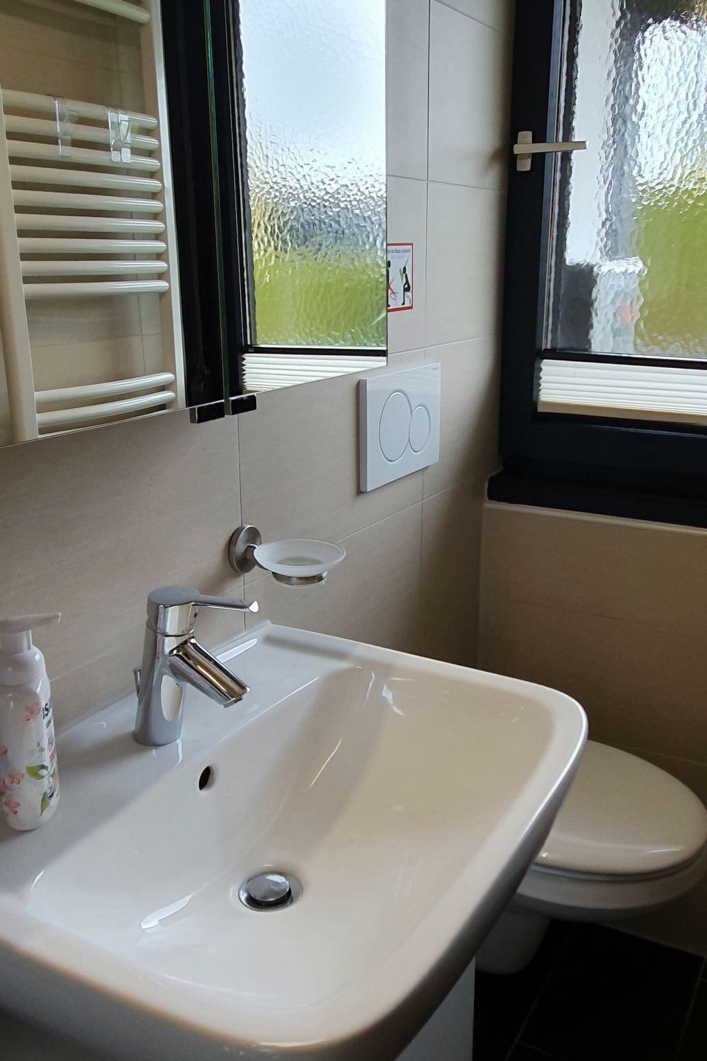 Une salle de bain avec un lavabo blanc, des toilettes, une fenêtre avec des stores et un porte-serviettes.