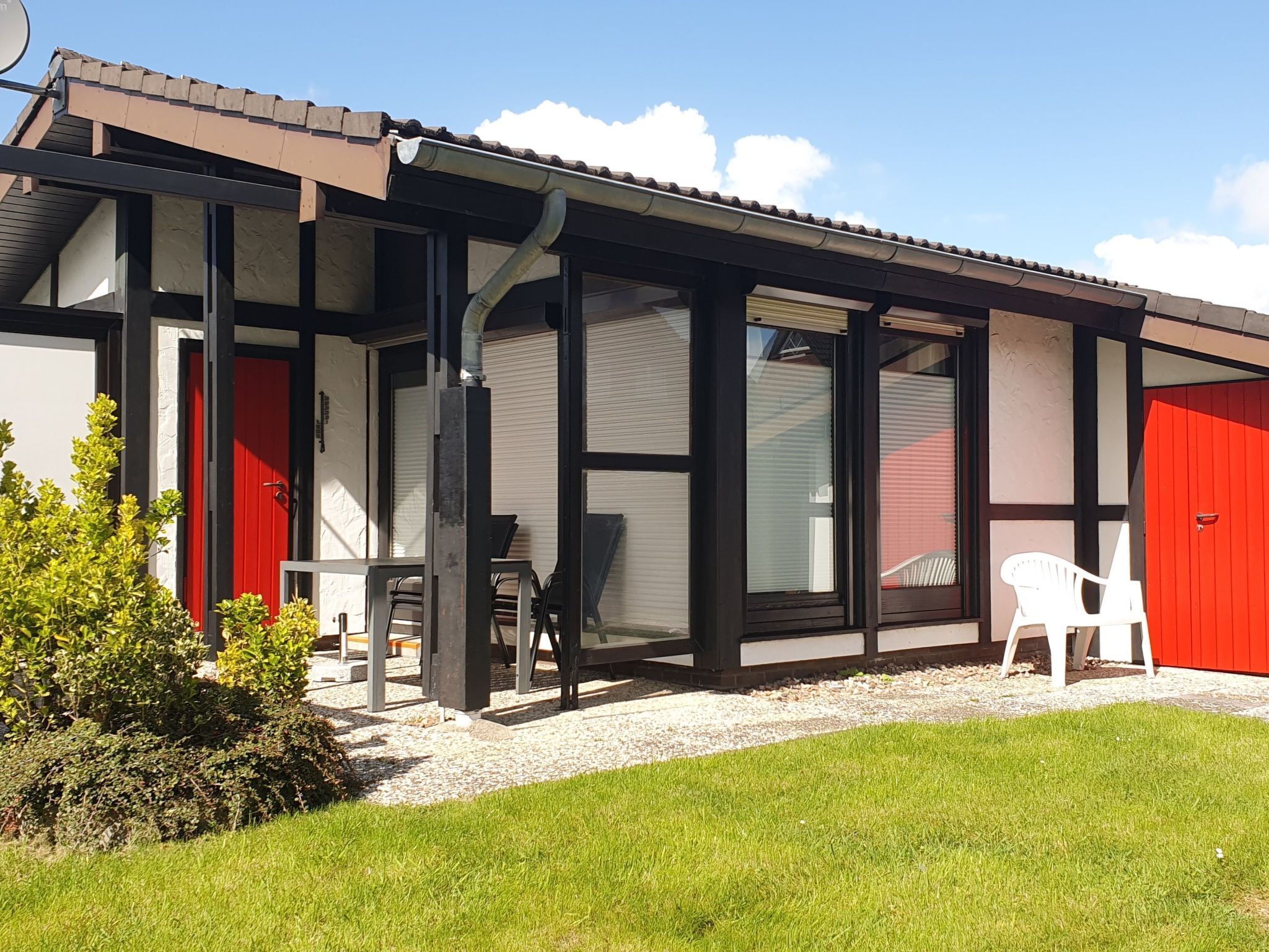 A modern building with large windows, a red door, and a covered outdoor area with chairs.