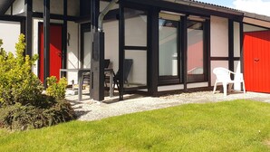 Un edificio moderno con amplios ventanales, una puerta roja y un área exterior cubierta con sillas.